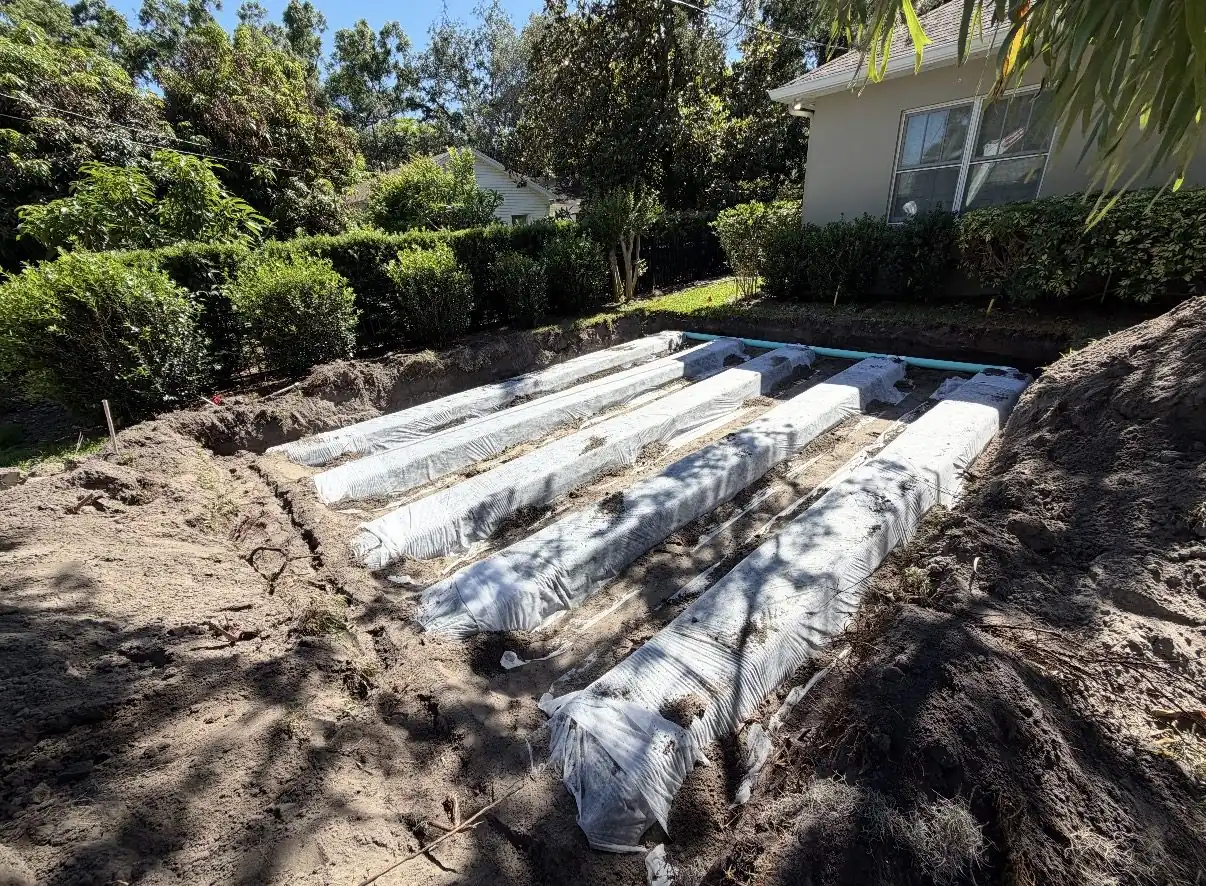 New drain field installation with chambers laid in open trenches beside a house