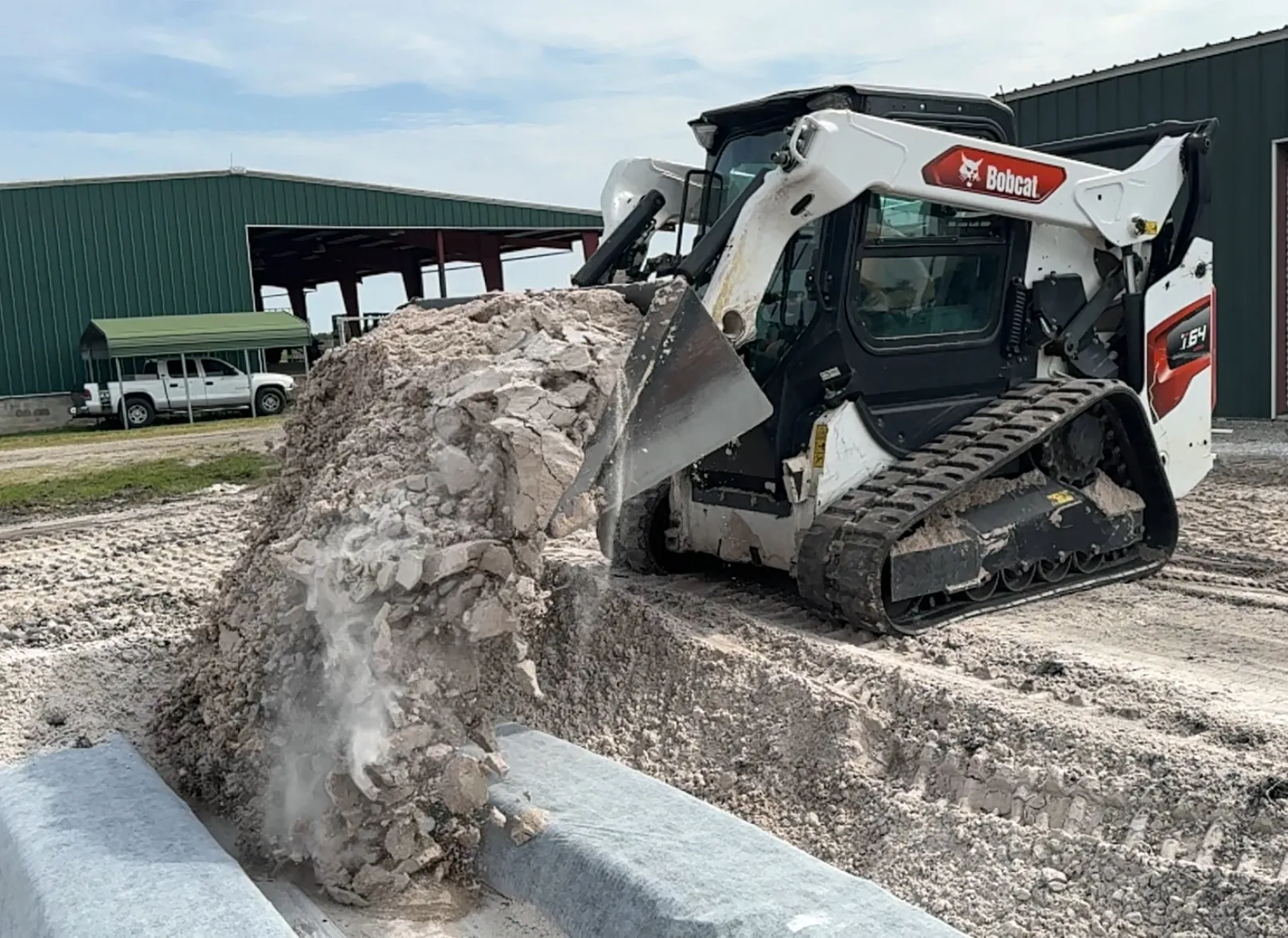 Bobcat track loader dumping rock into a trench beside drain field chambers