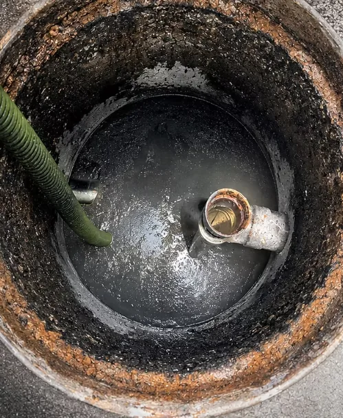 Open round grease trap interceptor with a pump-out hose during cleaning