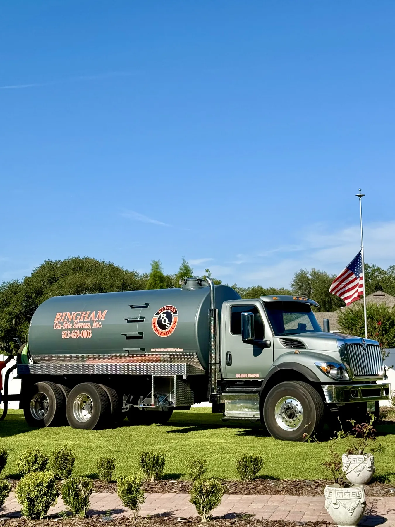 Bingham On-Site Sewers pump truck with 813-659-0003 on the tank, parked on grass beside a U.S. flag